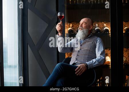 Male cavist sitting in a chair and looking at a glass of wine in his hand. Stock Photo