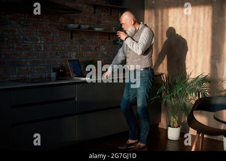 business man with a glass of wine checking his email in his kitchen . Stock Photo