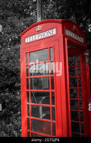 Traditional old red telephone box, selective color, close-up. Vintage British phone booth on black and white tree background. Stock Photo