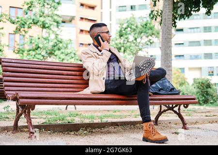 Young business man working with his laptop on a park bench while talking on the phone Stock Photo
