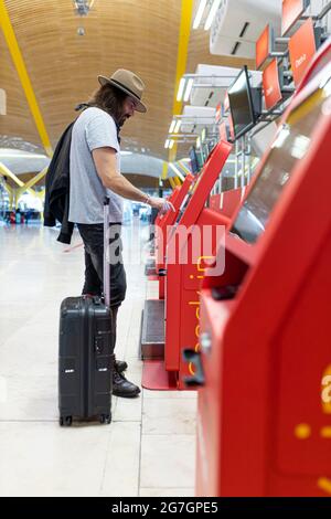 Young man with beard and long hair and hat buying airline tickets at the airline's automatic terminal Stock Photo