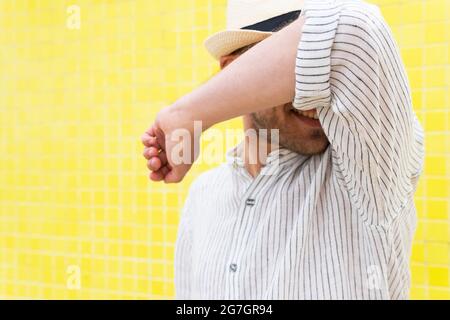 Unrecognizable guy in stylish summer outfit and hat doing no gesture and hiding face from camera against yellow wall Stock Photo