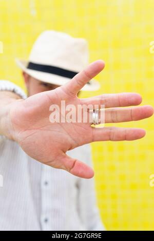Unrecognizable guy in stylish summer outfit and hat doing no gesture and hiding face from camera against yellow wall Stock Photo