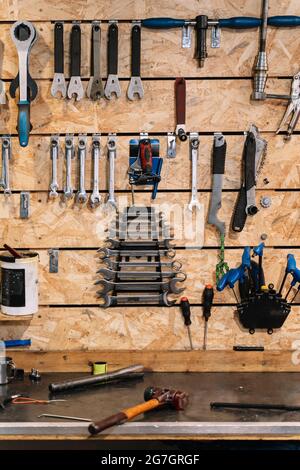 Various metal tools hanging in rows on wooden wall in shabby bicycle repair service Stock Photo
