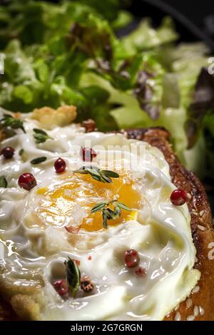 Fried egg on brioche served on tray with fresh lettuce for appetizing breakfast on black background Stock Photo