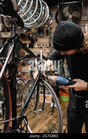 Professional skilled male mechanic using electric screwdriver while installing part of bicycle in workshop Stock Photo