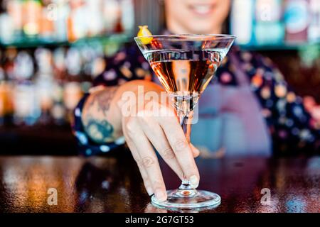 Anonymous cheerful female barkeeper with glass of refreshing vermouth standing at counter in bar Stock Photo