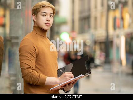 Focused ethnic male entrepreneur standing in street and writing on paper n folder Stock Photo