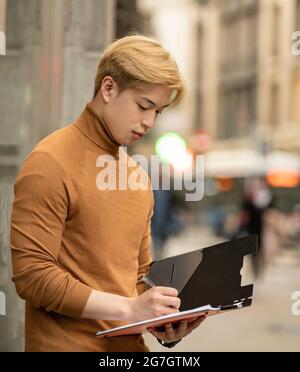 Focused ethnic male entrepreneur standing in street and writing on paper n folder Stock Photo