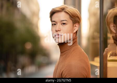 Side view of handsome Asian male model with blond hair looking at camera in city street Stock Photo