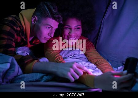 Happy multiracial man and Woman smiling resting and browsing cellphone in tent at night Stock Photo