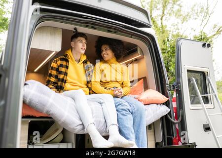 Happy black Woman smiling and holding hands with boyfriend while sitting on bed inside van on weekend day in nature Stock Photo
