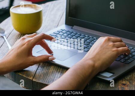 Cropped unrecognizable female freelancer typing on laptop keyboard while working on remote project on cafe terrace Stock Photo