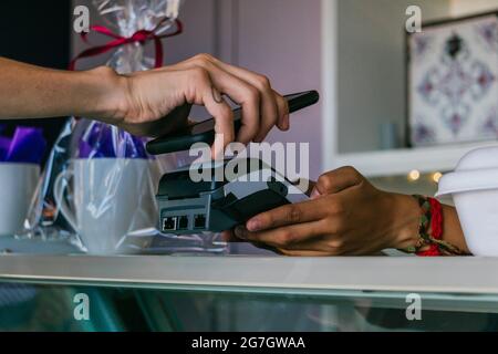 Crop anonymous customer making contactless payment on POS terminal with mobile phone in store Stock Photo