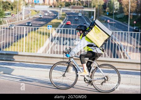 Side view of female courier with thermal bag riding bike on bridge while delivering food in city Stock Photo