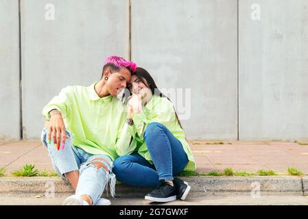 Gay man with pink hair and smiling Woman sitting in street and holding hands Stock Photo