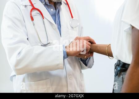Crop of anonymous senior male doctor measuring pulse of black female patient during check up in hospital Stock Photo