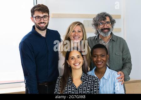 Delighted multiracial female colleagues looking at camera and smiling while sitting in workplace together Stock Photo
