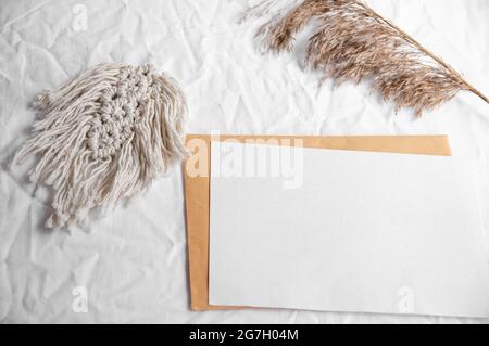 Envelope, macrame, pampas grass. Simple minimal flat lay on white textile with dry earth color neutral beige with macrame and dry reeds, pampas grass. Stock Photo