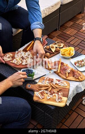 From above of crop anonymous men sitting at table with various delicious appetizer placed on terrace Stock Photo