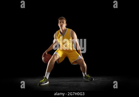 Basketball player with a ball in action and motion isolated on dark black studio background. Advertising concept. Strong Caucasian athlete practicing Stock Photo