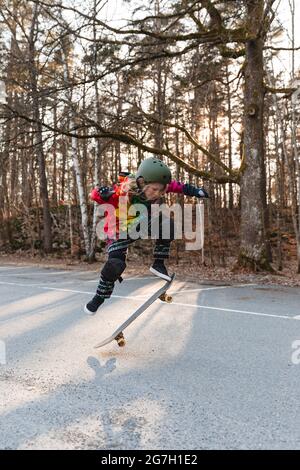 Energetic teenage girl in protective gear jumping above ground with skateboard and performing trick Stock Photo