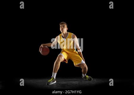 Basketball player with a ball in action and motion isolated on dark black studio background. Advertising concept. Strong Caucasian athlete practicing Stock Photo