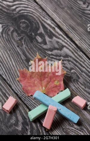 School accessories. Crayons of different colors lie on the pine boards. Nearby are fallen maple leaves. Stock Photo