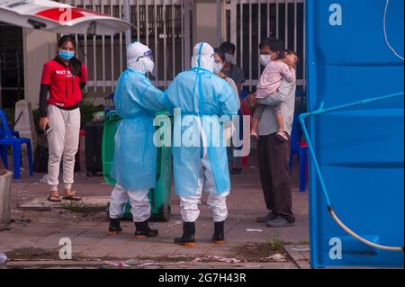 Phnom Penh, Cambodia. July 14th, 2021. for almost 5 months Phnom Penh has been battling a COVID - 19 surge. A Cambodian mother, father & their young daughter have all tested positive for the virus at a mass testing site. 2 EMTs / medics in full PPE explain the situation to them. Cambodians who test positive cannot leave the testing site & need to call a friend or a relative to pick up thier personal belongings for the hospital stay. credit: Kraig Lieb / Alamy Live News Stock Photo