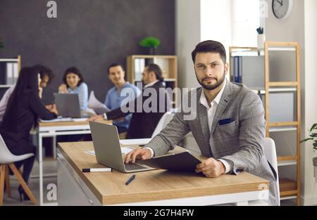 Portrait of confident young businessman sitting at office desk with laptop computer Stock Photo