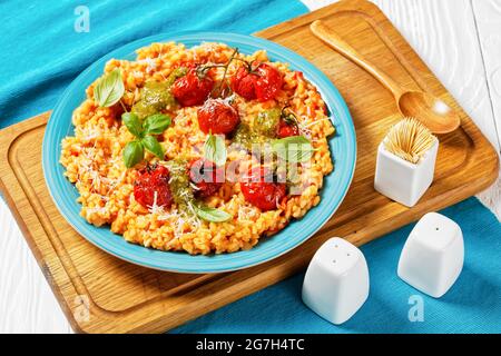 creamy tomato risotto with cherry tomatoes and sauce pesto on a blue plate on a cutting board, close-up Stock Photo