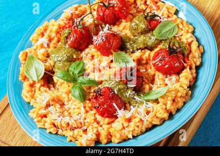 close-up of creamy tomato risotto with cherry tomatoes and sauce pesto on a blue plate Stock Photo