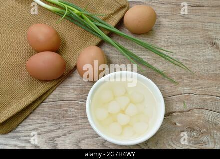 pickled single garlic in salt water on cup with raw egg and spring onion on table Stock Photo
