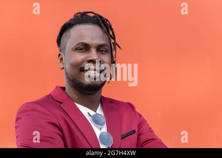 portrait of a stylish black businessman posing looking at camera with arms crossed in front of red background, copy space for text Stock Photo