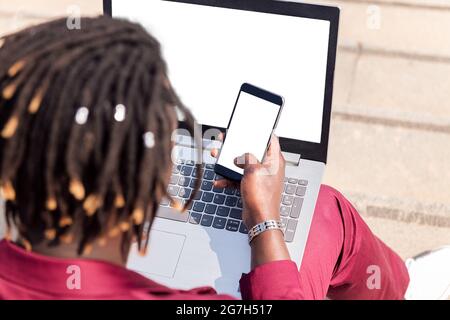 rear view of an unrecognizable black businessman using a smart phone and computer laptop, technology and remote work concept, copy space for text Stock Photo