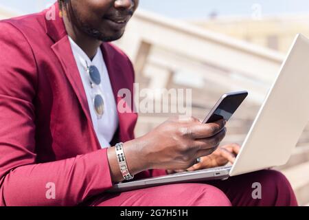 unrecognizable black businessman using a smart phone and computer laptop, technology and remote work concept, copy space for text Stock Photo