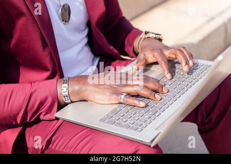 detail of the hands of an unrecognizable african man working with his laptop computer sitting on a staircase in the city, concept of technology and re Stock Photo