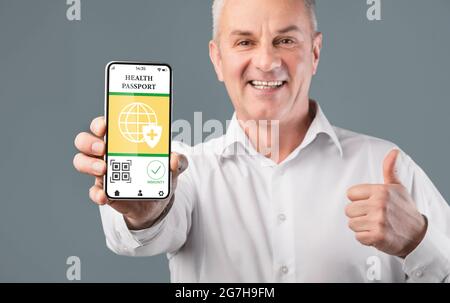 Health Passport. Smiling senior older man holding smartphone with digital pass in hand, showing mobile application with his status and thumbs up gestu Stock Photo