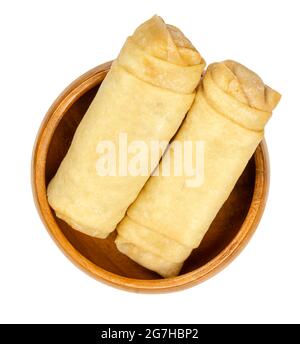 Unfried spring rolls, in a wooden bowl. Two spring rolls, ready to fry. Filled and rolled wrappers, appetizers in Asian cuisine. Close-up, from above. Stock Photo