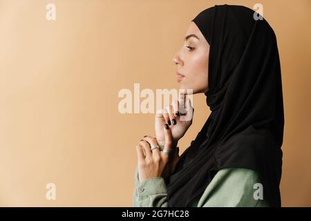 Portrait of a young muslim woman in hijab standing over beige background side view portrait Stock Photo