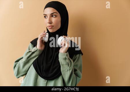 A confident muslim woman wearing black hijab holding her headphones in the orange studio Stock Photo
