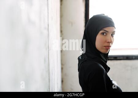 Young muslim sportswoman in hijab looking at camera while standing indoors Stock Photo