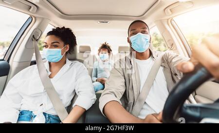African American Family Wearing Face Masks Riding Car Traveling By Auto. Covid-19 Pandemic Outbreak And Coronavirus Protection. Safe Summer Road Trip Stock Photo