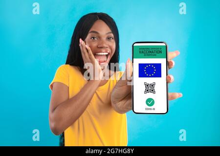 Excited Vaccinated African American Woman Showing Phone With Certificate Of Covid-19 Vaccination After Getting Vaccinated On Blue Studio Background. C Stock Photo