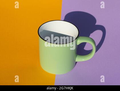 An empty green mug with harsh shadow on yellow and purple background. Copy space. Close up. Stock Photo