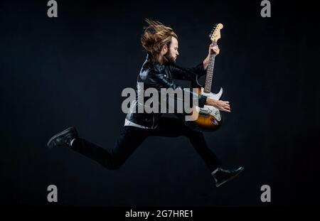 emotional bearded rocker in leather jacket. man long hair play electric guitar. Stock Photo