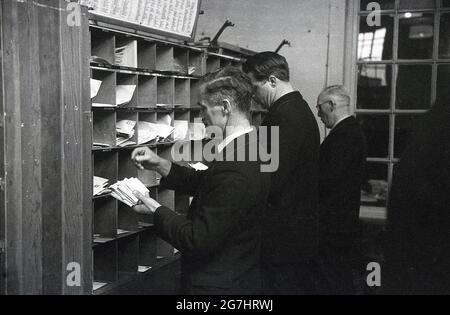 1950s, historical, three male GPO workers sorting out letters or mail into the cubby-holes on a shelf divided up into the district dfferent streets, London, England, UK. Stock Photo