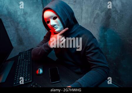 Anonymous hacker wearing face mask working on computer in dark room Stock Photo