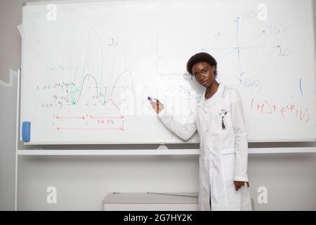 African American woman univercity student writing on blackboard with marker. Stock Photo
