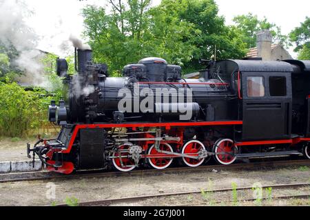 Old steam engine locomotive move on trail. Narrow-gauge railway retro travel. Stock Photo